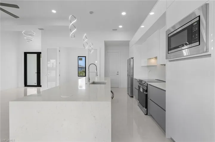 Kitchen featuring ceiling fan, sink, a center island with sink, white cabinetry, and stainless steel appliances