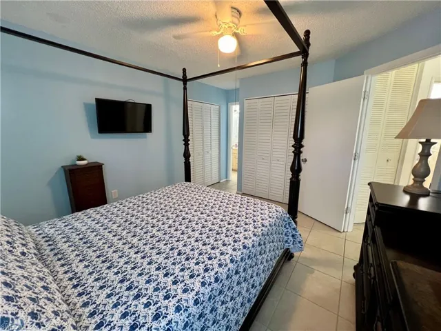 Primary bedroom with tiled floor with a textured ceiling, ceiling fan, and multiple closets