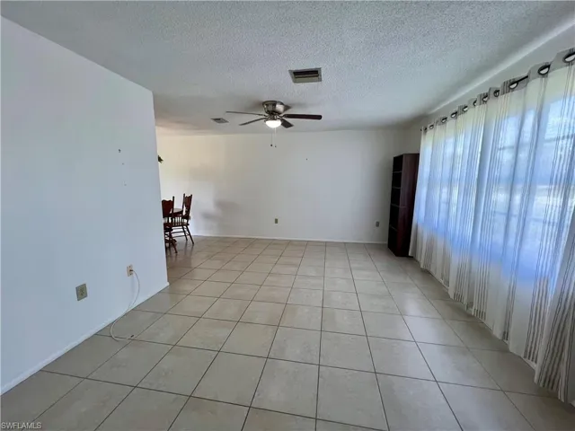 Living room featuring ceiling fan, light tile patterned floors, and a textured ceiling
