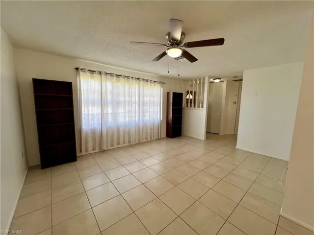 Living room featuring a textured ceiling, light tile patterned flooring, and ceiling fan