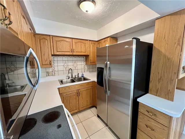 Kitchen with light tile patterned floors, sink, a textured ceiling, backsplash, and stainless steel refrigerator with ice dispenser