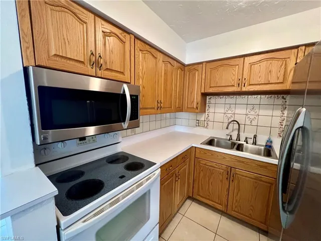 Kitchen featuring light tile patterned flooring, appliances with stainless steel finishes, sink, and decorative backsplash