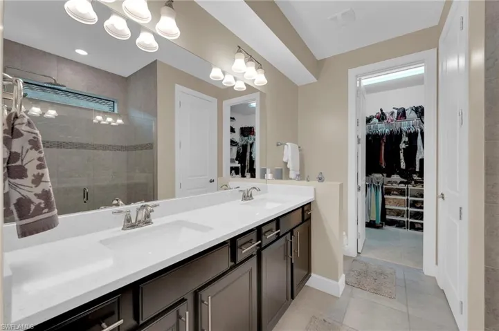 Bathroom featuring light tile patterned floors, double vanity, a spacious closet, and a stall shower
