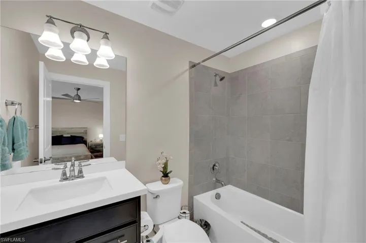 Ensuite bathroom featuring shower / bathtub combination with curtain, vanity, and ceiling fan