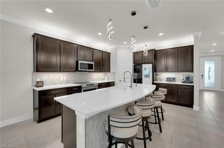 Kitchen featuring dark brown cabinets, tasteful backsplash, ornamental molding, a kitchen bar, and stainless steel appliances
