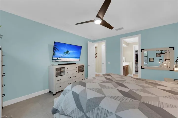Bedroom featuring a ceiling fan, crown molding, light tile patterned floors, and connected bathroom