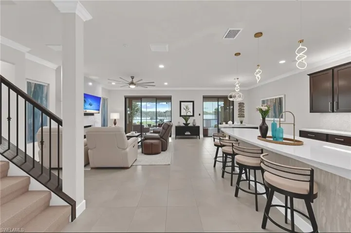 Kitchen with ornamental molding, a kitchen bar, pendant lighting, light stone counters, and recessed lighting