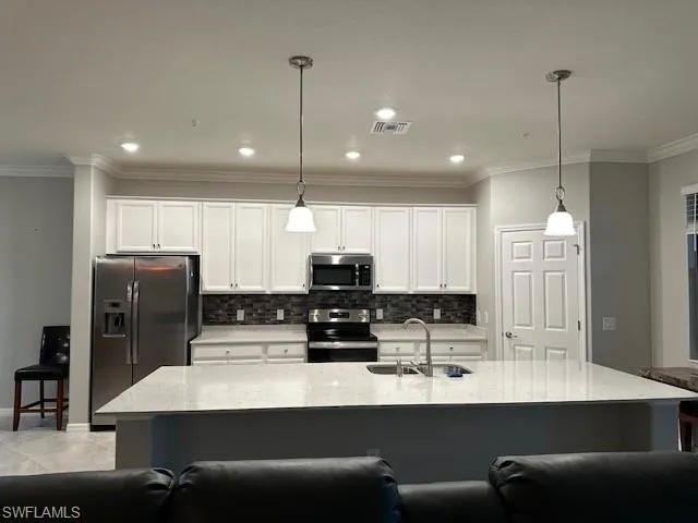 Kitchen with sink, light stone counters, hanging light fixtures, a center island with sink, and stainless steel appliances