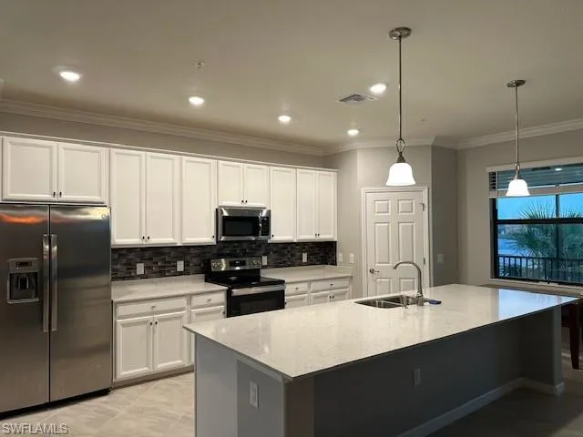 Kitchen with sink, hanging light fixtures, stainless steel appliances, white cabinets, and a center island with sink