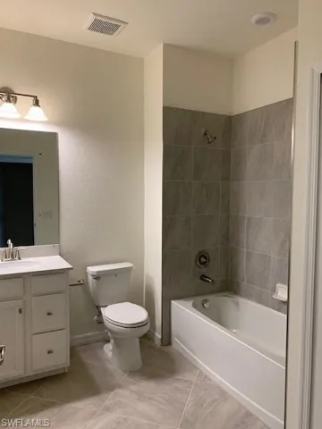 Full bathroom with vanity, tile patterned floors, toilet, and tiled shower / bath
