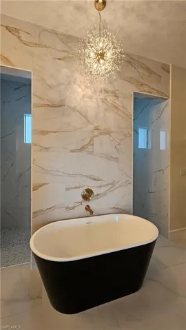 Full bathroom with a soaking tub, a chandelier, and stone wall
