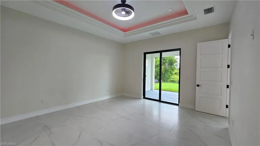 Primary bedroom featuring a raised ceiling, light marble finish flooring, and ornamental molding