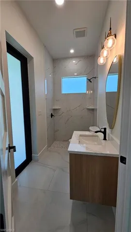 Guest bathroom with a marble-like finish shower, vanity, and recessed lighting
