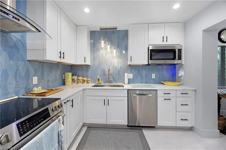 Kitchen with stainless steel appliances, white cabinetry, wall chimney range hood, tasteful backsplash, and light stone counters