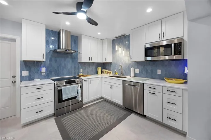 Kitchen featuring appliances with stainless steel finishes, wall chimney exhaust hood, white cabinets, ceiling fan, and backsplash