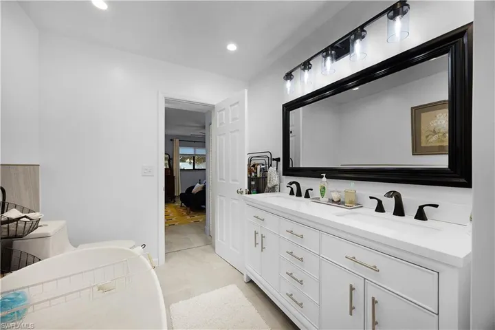 Ensuite bathroom featuring double vanity, recessed lighting, light tile patterned floors, and a bathtub