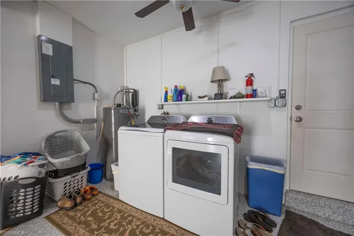 Washroom featuring electric panel, washer and clothes dryer, a ceiling fan, and water heater