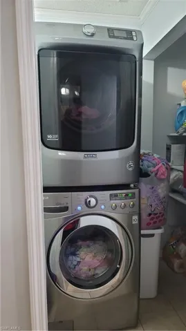 Washroom with stacked washer / drying machine, crown molding, and light tile patterned floors