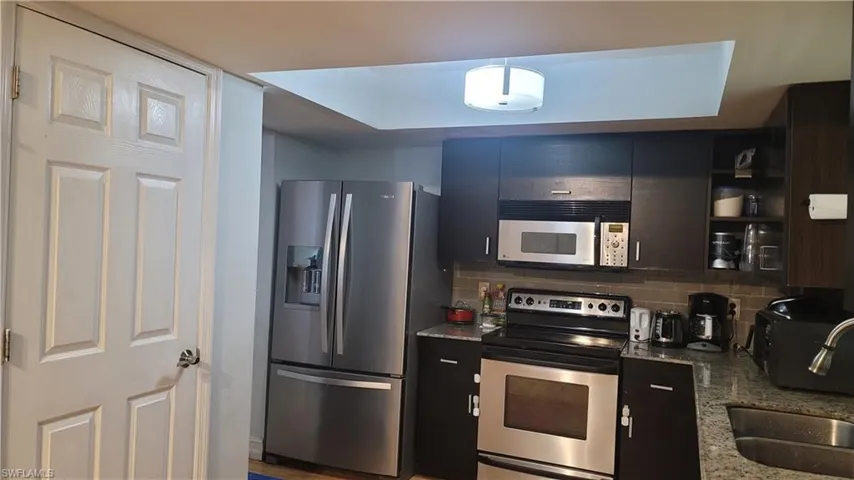 Kitchen with appliances with stainless steel finishes, open shelves, dark stone countertops, and decorative backsplash