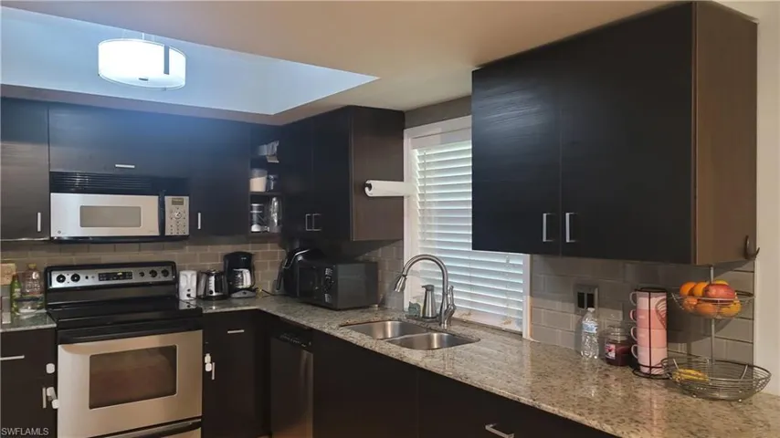 Kitchen featuring stainless steel electric range, light stone countertops, dark cabinets, decorative backsplash, and modern cabinets
