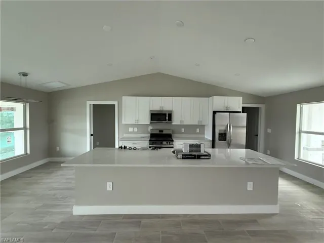 Kitchen with appliances with stainless steel finishes, vaulted ceiling, a large island with sink, decorative light fixtures, and white cabinets