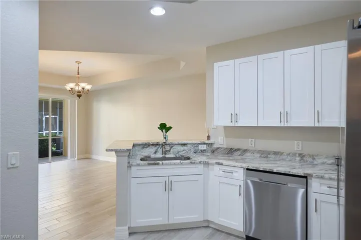 Kitchen with white cabinetry, light stone counters, kitchen peninsula, light wood-tile flooring, and stainless steel dishwasher