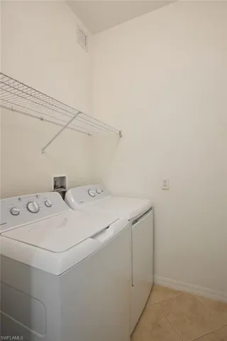 Clothes washing area with separate washer and dryer and light tile patterned flooring