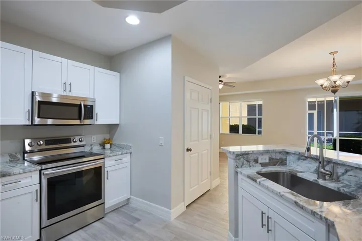 Kitchen with sink, light hardwood / wood-tile flooring, white cabinetry, appliances with stainless steel finishes, and ceiling fan with notable chandelier