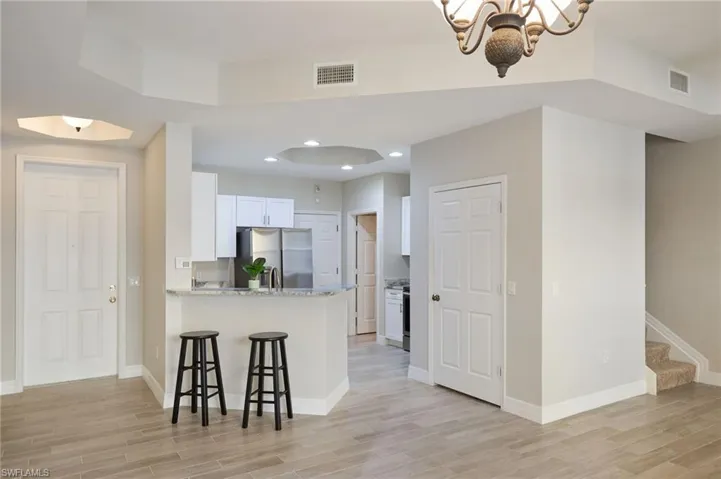 Kitchen with white cabinets, stainless steel refrigerator, kitchen peninsula, light stone countertops, and a notable chandelier