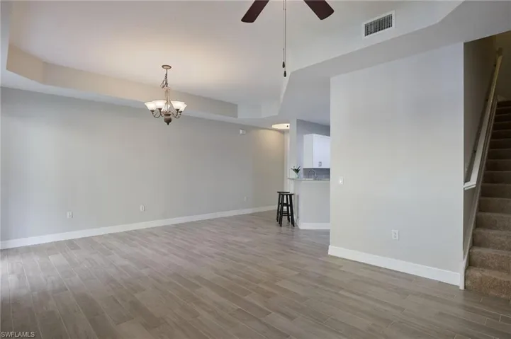 Unfurnished living room featuring light wood-tile, ceiling fan with notable chandelier, a tray ceiling, and sink