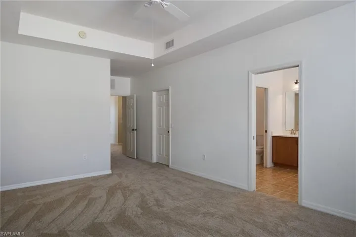 Unfurnished bedroom with ensuite bath, light carpet, and ceiling fan