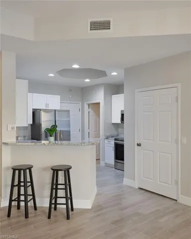 Kitchen featuring kitchen peninsula, light hardwood / wood-tile flooring, white cabinetry, appliances with stainless steel finishes, and a breakfast bar area