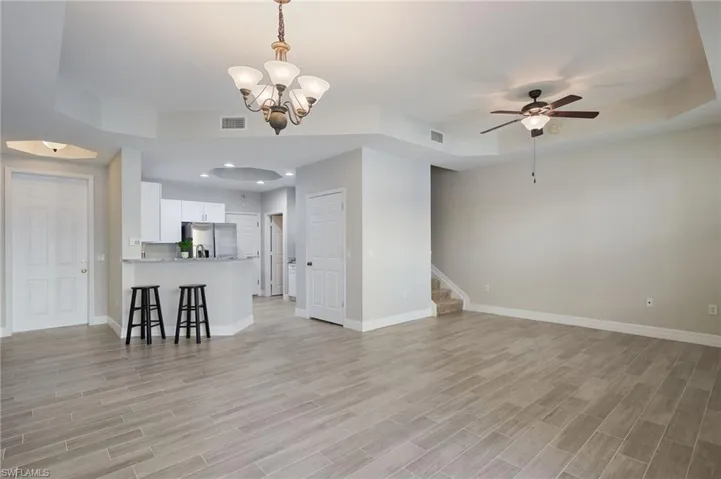 Unfurnished living room with ceiling fan, notable chandelier, light hardwood / wood-tile  floors, and a tray ceiling