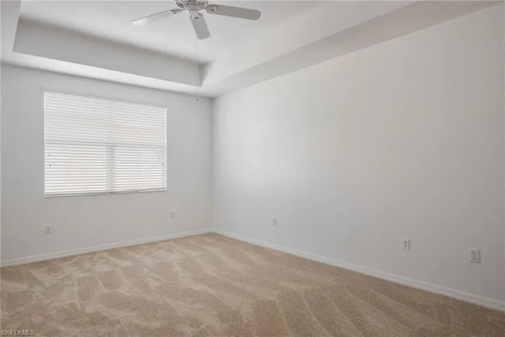 Carpeted empty room with ceiling fan and a raised ceiling