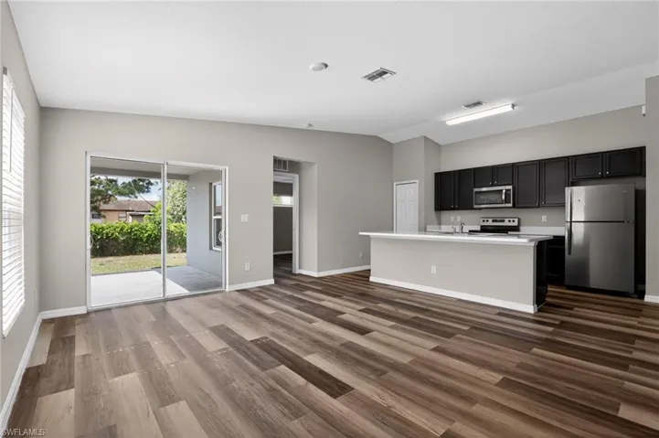 Open-concept living area featuring wood-finish flooring, a kitchen island with seating, dark wood cabinetry, and stainless steel appliances