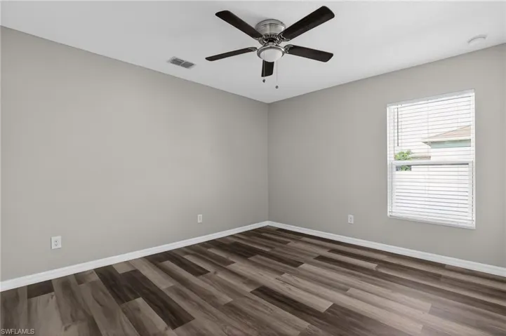 Spacious room featuring wood-finish flooring, light gray walls, a ceiling fan with integrated lighting, and a window with blinds