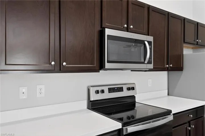 Kitchen featuring dark wood-finish cabinetry, stainless steel appliances, and white countertops