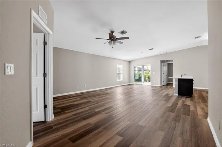Spacious interior featuring wood-finish flooring, neutral paint tones, a ceiling fan, sliding glass door access to the exterior, and a built-in counter with sink