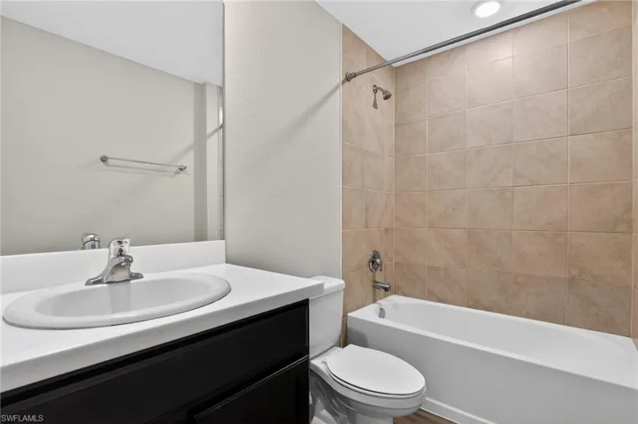 Bathroom featuring a combination shower and tub with beige wall tiling, a dark wood-finish vanity with an integrated white sink, a chrome faucet, and a large wall-mounted mirror