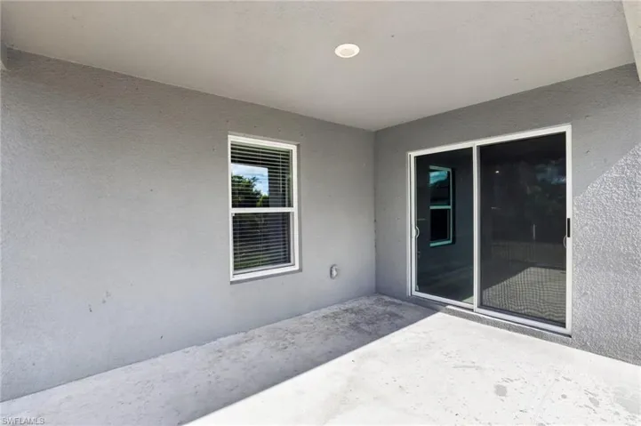 Covered patio featuring a sliding glass door, single window with blinds, stucco exterior, concrete flooring, and recessed lighting