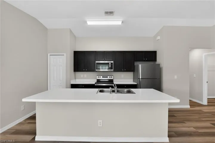 Kitchen featuring an expansive island with an undermount double-basin sink, dark cabinetry, light countertops, and stainless steel appliances