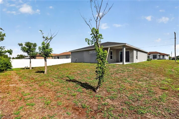 Expansive rear yard featuring a partial white privacy fence and a rear covered patio with concrete flooring