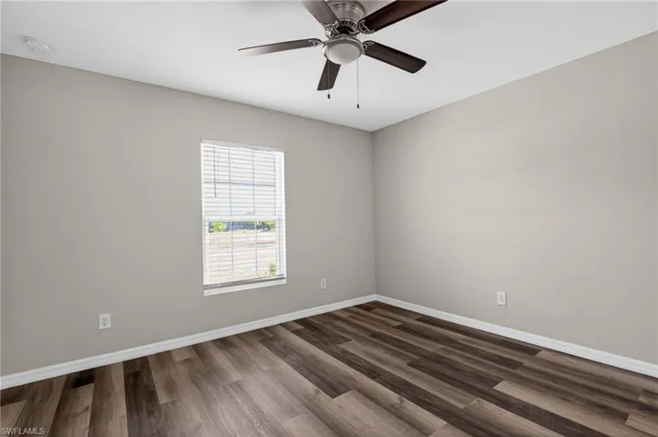 Room featuring wood-finish flooring, neutral wall paint, white baseboards, a window with horizontal blinds, and a ceiling fan with integrated lighting
