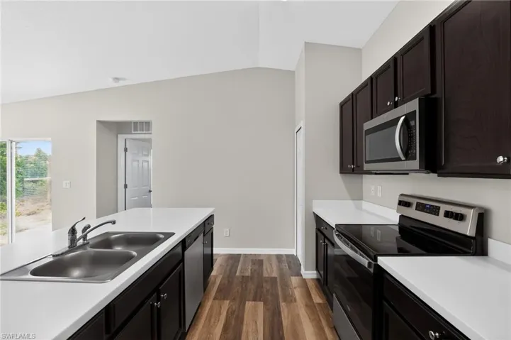Modern kitchen featuring dark wood-finish cabinetry, stainless steel appliances, white countertops, a double basin sink, and wood-finish flooring