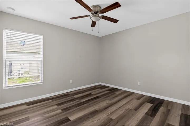 Spacious room featuring wood-finish flooring, neutral-toned walls, and a ceiling fan with integrated lighting