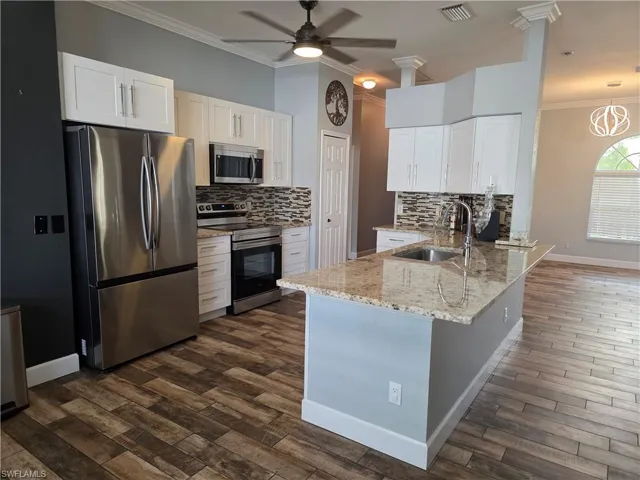 Kitchen featuring crown molding, stainless steel appliances, backsplash, light stone counters, and white cabinets