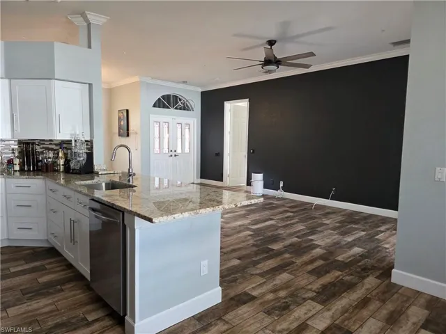 Kitchen featuring white cabinets, ornamental molding, dishwasher, light stone counters, and a peninsula
