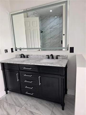 Bathroom featuring light marble finish floors, a marble finish shower, and double vanity
