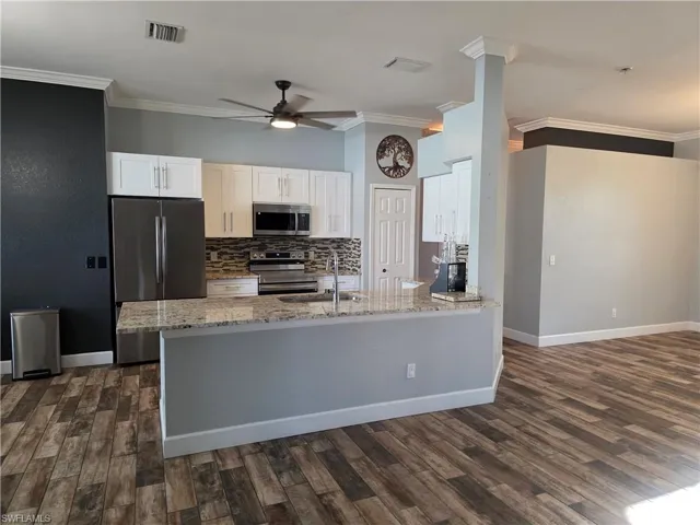 Kitchen featuring white cabinets, appliances with stainless steel finishes, ornamental molding, backsplash, and light stone countertops
