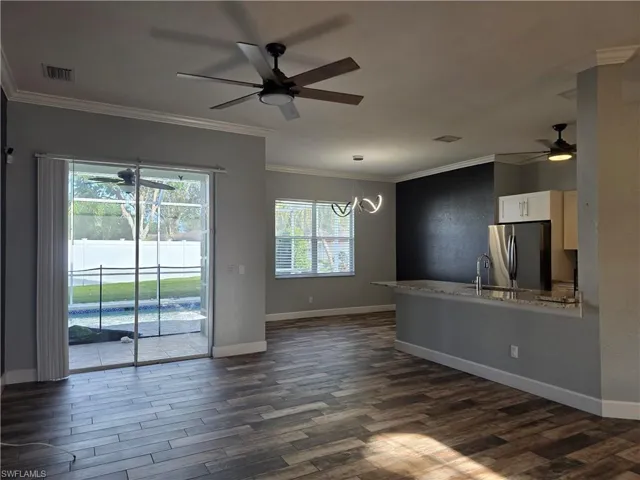 Unfurnished living room featuring ceiling fan, crown molding, dark wood-style floors, and a chandelier